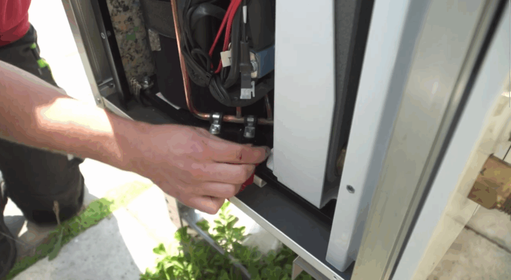 Technische Feineinstellungen an einer geöffneten Wärmepumpen-Außeneinheit, mit sichtbaren Komponenten und Leitungen.