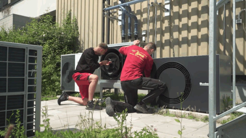 Zwei Techniker überprüfen und warten die Ventilator-Außeneinheit einer Wärmepumpenanlage.
